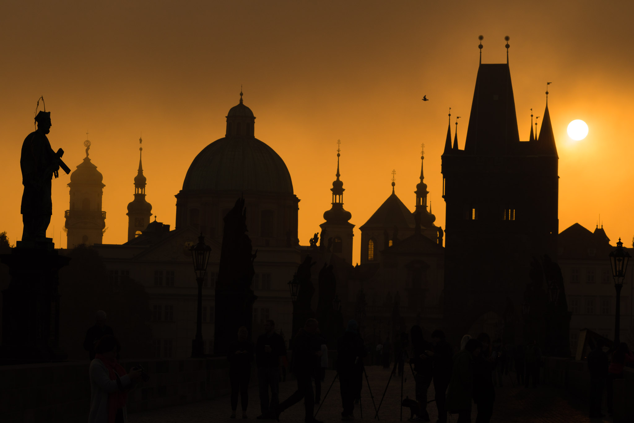 Silhouettes of Prague towers and statues on Charles bridge during sunrise